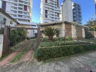 Foto da fachada de uma residência com portão de metal e vegetação.