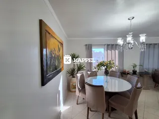 Uma sala de jantar com mesa redonda e cadeiras estofadas é visível na imagem.