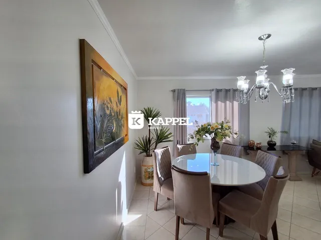 Uma sala de jantar com mesa redonda e cadeiras estofadas é visível na imagem.