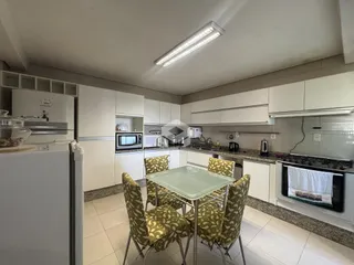 Cozinha e sala de jantar com armários brancos e mesa de vidro.