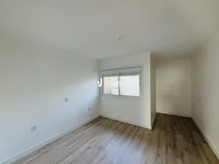 Ambiente interno de uma sala com piso de madeira clara e paredes brancas.