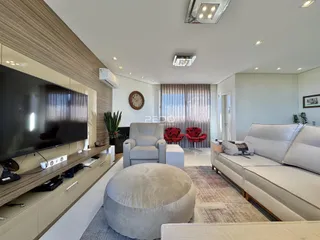 Sala de estar moderna com sofá, poltronas e pufe em um ambiente claro.