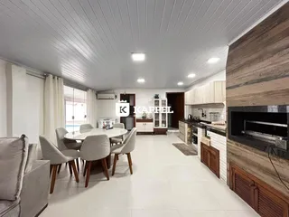 Foto interna de uma sala de jantar e cozinha com piso claro e iluminação abundante.