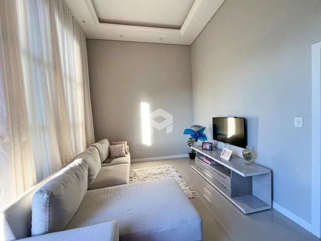 Sala de estar moderna com grandes janelas e cortinas brancas.