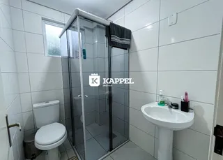 Banheiro com box de vidro, vaso sanitário e pia, com revestimento de azulejos brancos.