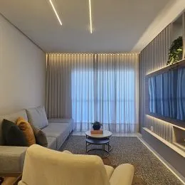 Sala de estar com sofá e cortinas claras em um ambiente interno.