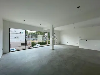 Espaço interno amplo com piso de concreto e grandes janelas de vidro.