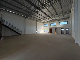 Vista interna de um grande espaço industrial com teto metálico e piso de concreto.