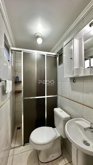 Banheiro com revestimento cerâmico claro e box de vidro.