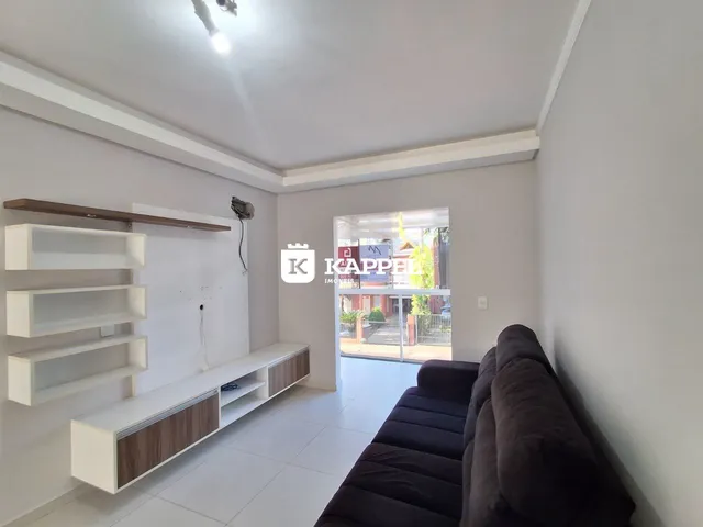 Sala de estar clara com sofá escuro e estantes brancas em um ambiente bem iluminado.