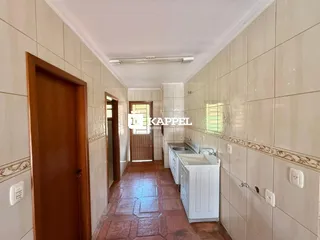 Corredor interno com paredes de azulejo claro e área de cozinha visível.