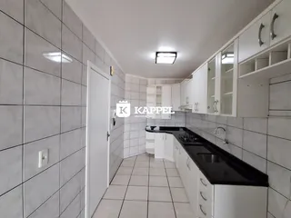 Cozinha com armários brancos e bancada escura em um corredor com piso de cerâmica.