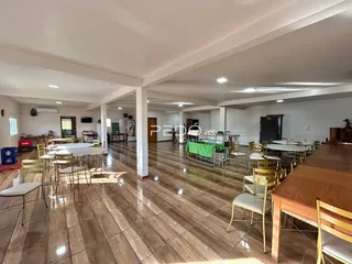 Ambiente interno de uma sala ampla com piso de madeira e mesas dispostas.
