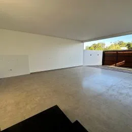 Foto de um ambiente interno amplo com piso de concreto liso e paredes brancas.