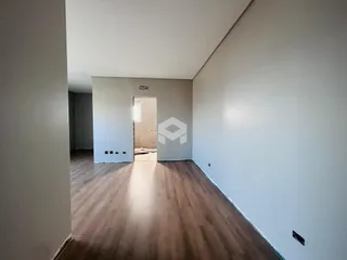 Um corredor interno com piso de madeira e paredes brancas.