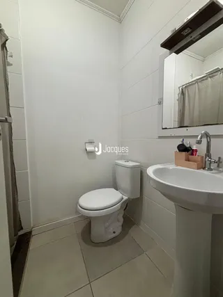 Foto interna de um banheiro com azulejos brancos e louças sanitárias.