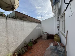 Vista externa de um pátio com paredes brancas e piso de tijolos vermelhos.