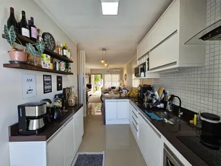 Vista interna de uma cozinha moderna com armários brancos e bancadas escuras.