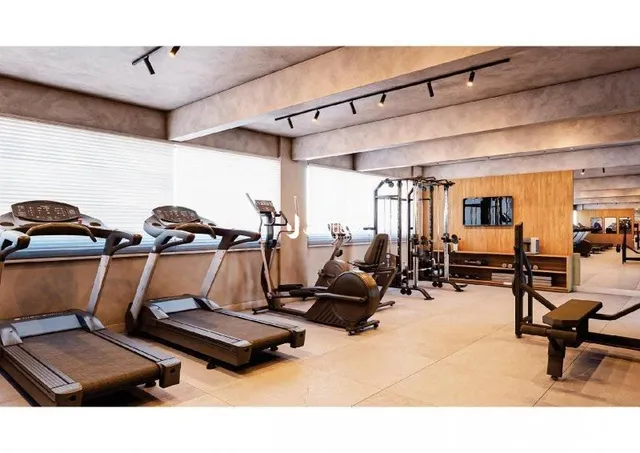 Imagem de uma área de ginástica interna com esteiras e equipamentos de treino.