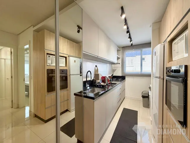 Cozinha moderna com armários brancos e bancada escura em apartamento em Lajeado.