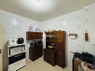 Cozinha com armários de madeira e piso cerâmico nas paredes brancas.