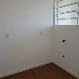 Foto de um canto interno com parede branca e piso de madeira.