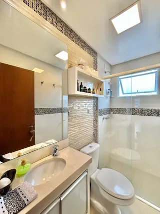 Interior de um banheiro com revestimento cerâmico e box de vidro.
