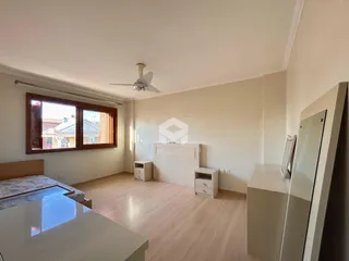 Quarto com piso de madeira clara e janela de vista para a rua.