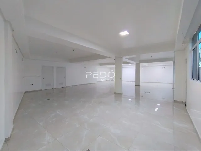 Vista interna de um grande espaço vazio com piso de cerâmica claro.