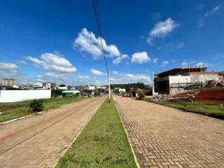 Vista de uma rua pavimentada com gramado e área de construção ao fundo.