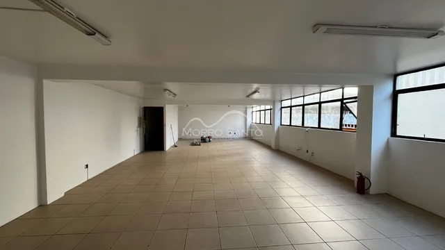 Vista interna de um corredor com piso de cerâmica e grandes janelas.
