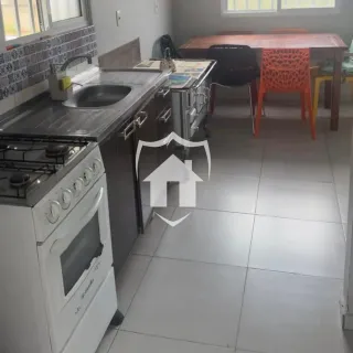 Vista interna de uma cozinha com bancadas escuras e mesa de jantar.