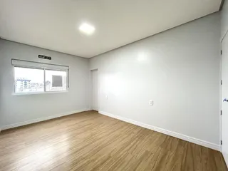 Ambiente interno de uma sala com piso de madeira clara e paredes brancas.