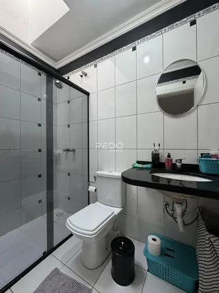 Foto do interior de um banheiro com box de vidro e revestimento branco.