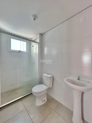 Interior de um banheiro com revestimento cerâmico e box de vidro.