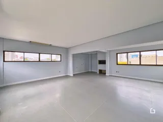 Foto de um ambiente interno vazio com paredes cinzas e grandes janelas.