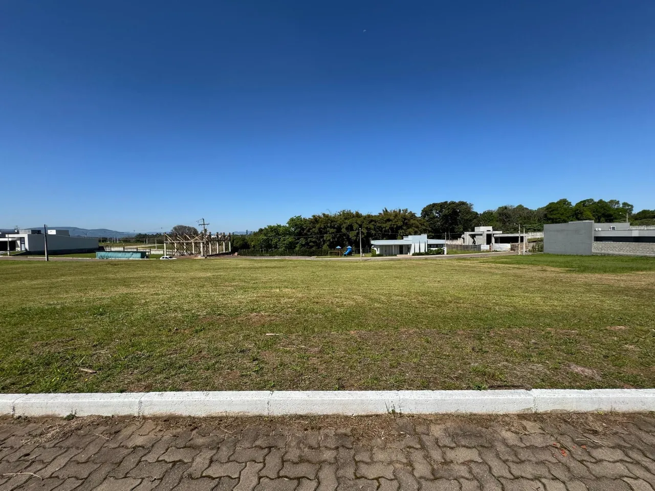 Vista externa de um terreno gramado com estruturas ao fundo.
