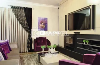 Sala de estar com sofá roxo e televisão montada na parede.