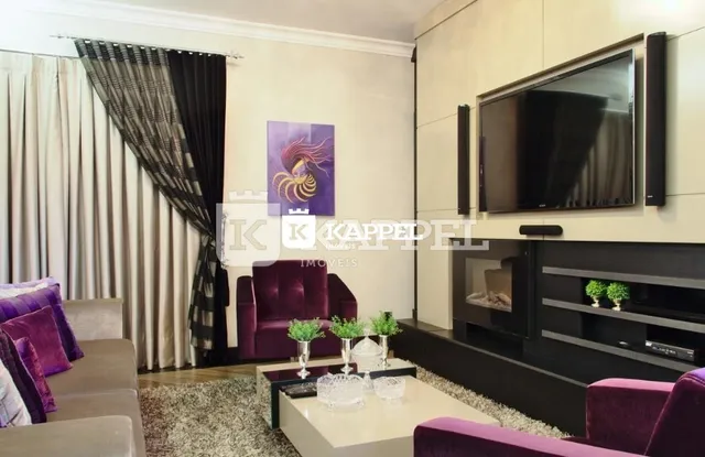 Sala de estar com sofá roxo e televisão montada na parede.