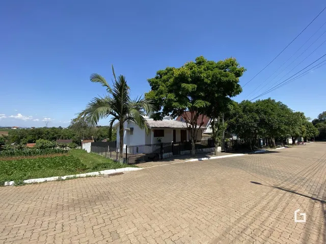 Vista da fachada de uma residência em Lajeado, Brasil, com árvores e área pavimentada na frente.