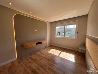 Sala de estar com piso de madeira clara e iluminação embutida na parede curva.