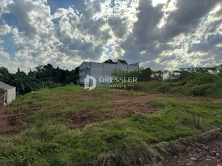 Vista externa de um terreno com vegetação rasteira e uma estrutura industrial ao fundo.
