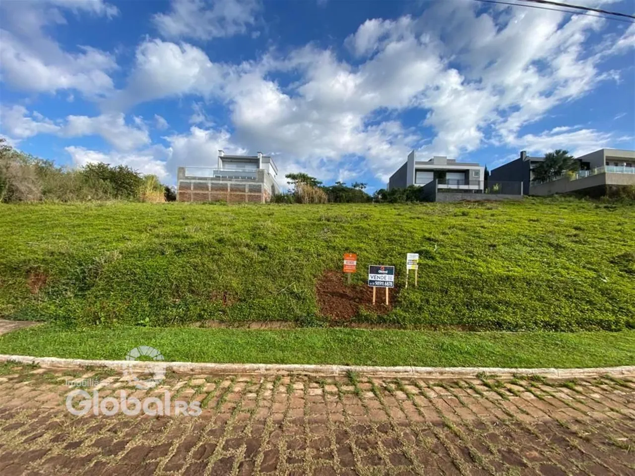 Vista externa de uma propriedade com terreno gramado e casas ao fundo.