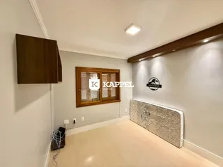 Foto interna de um quarto com piso de madeira clara e janela de madeira.