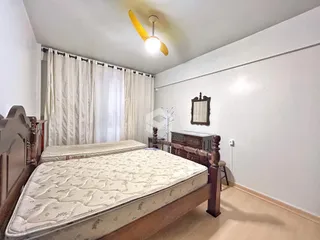 Quarto com cama de madeira e cortinas brancas.