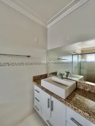 Banheiro com bancada de granito e armários brancos.