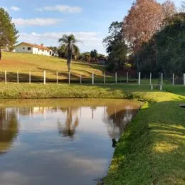 Vista de um corpo d'água com vegetação e gramados ao fundo.