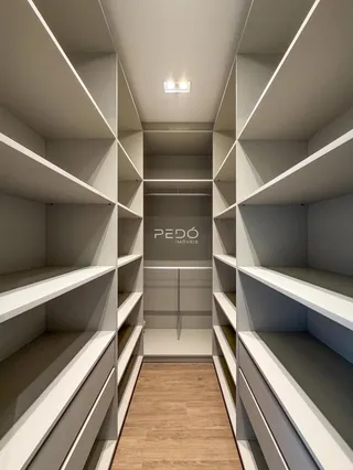 Corredor com prateleiras embutidas brancas e piso de madeira.