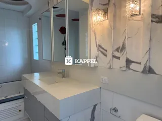 Banheiro moderno com bancada branca e revestimento em mármore.
