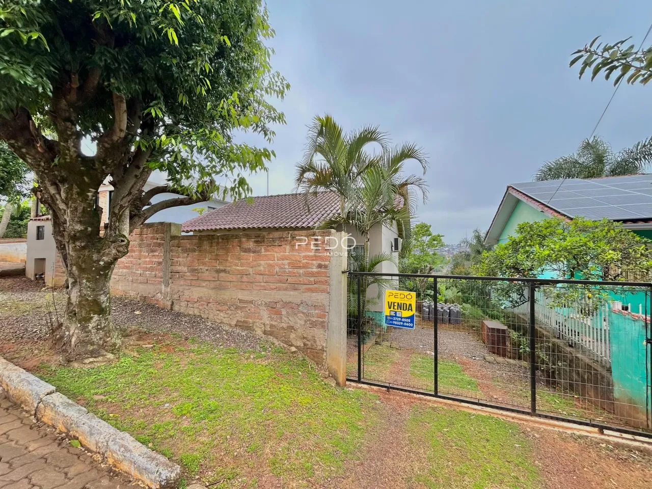 Vista externa de uma propriedade com muro de tijolos e cerca de metal.